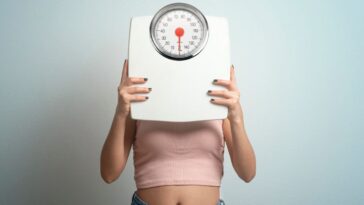 Young woman hides face behind a bathroom scale. Studio shot.