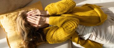 Tired woman lying on sofa while holding hands on her face.