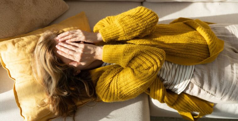 Tired woman lying on sofa while holding hands on her face.