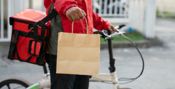 food in paper bag being delivered by person in red jacket on a bicycle