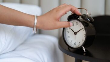 Close-up of a hand reaching for a classic alarm clock.