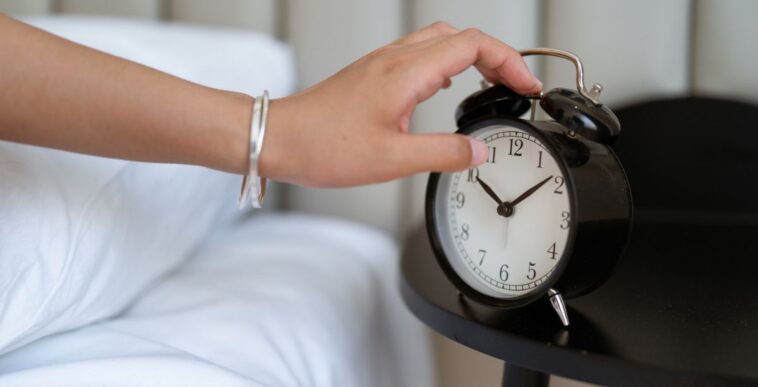 Close-up of a hand reaching for a classic alarm clock.