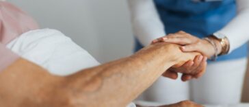 Close-up of caregiver holding senior client hand. Support from nurse to patient, taking care of elderly man in hospital. Emotional support and care in healthcare, hospice care.