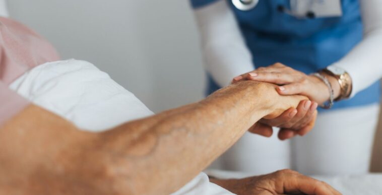 Close-up of caregiver holding senior client hand. Support from nurse to patient, taking care of elderly man in hospital. Emotional support and care in healthcare, hospice care.