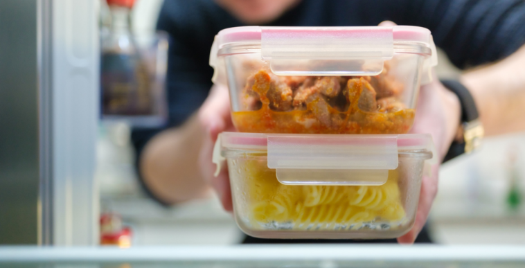 A man putting two tupperware containers full of leftovers in the fridge.