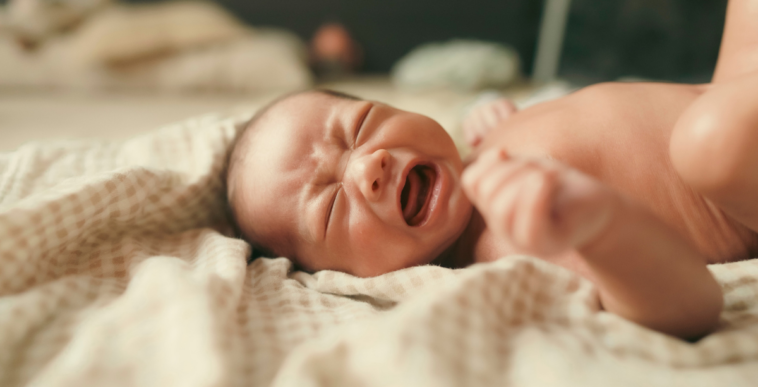 A baby lying on a bed an crying.