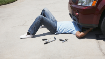 A man under the front of a car with tools laying by his side.