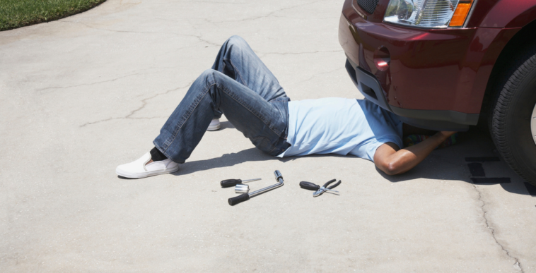 A man under the front of a car with tools laying by his side.