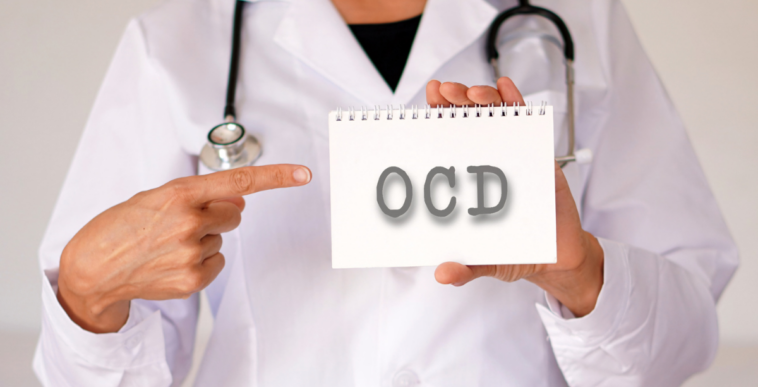 A person in a lab coat with a stethoscope around their shoulders holding a card that says OCD on it.