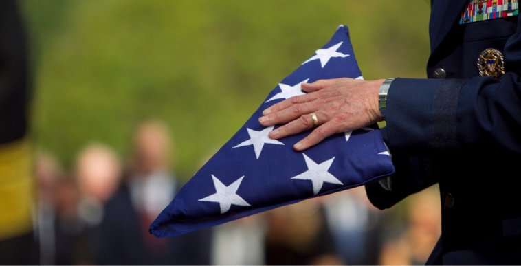 A man in a military uniform holding a folded American flag.
