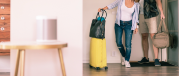 A couple entering a living room with luggage.