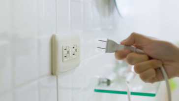 A hand unplugging a plug from a socket.