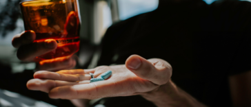 A person holding a glass of water in one hand and a pill in another.