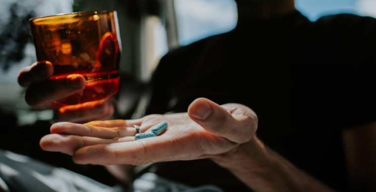 A person holding a glass of water in one hand and a pill in another.