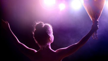 A woman on a stage holding out her arms and holding a bouquet of flowers.