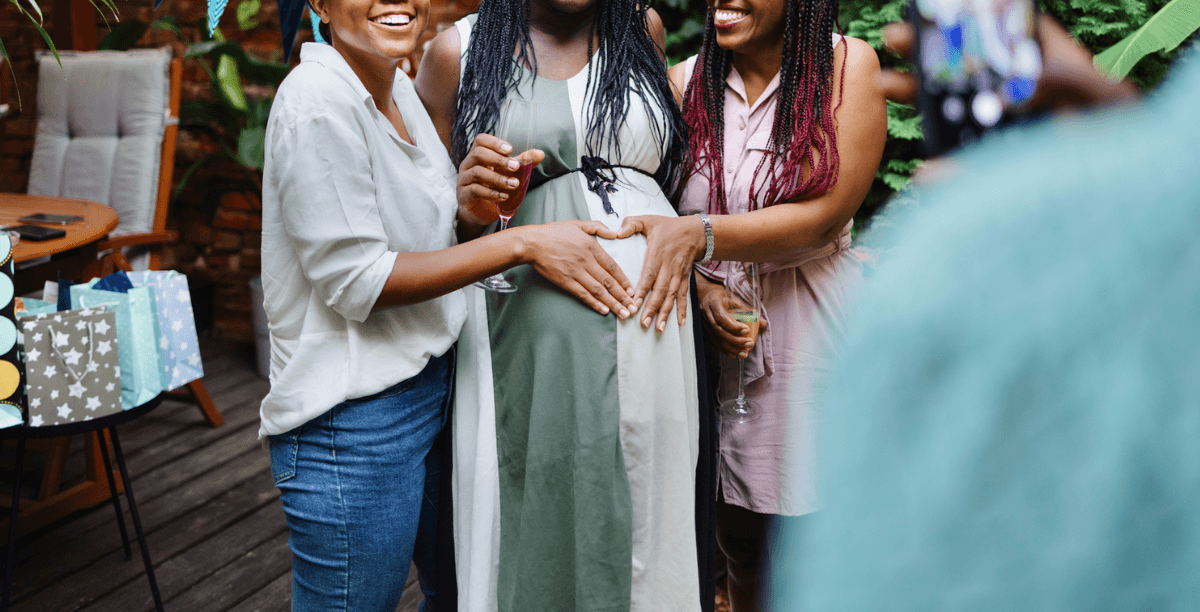 Two women putting their hands on a pregnant woman's baby bump.