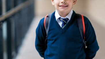 A young male student looking very happy at school wearing his uniform.