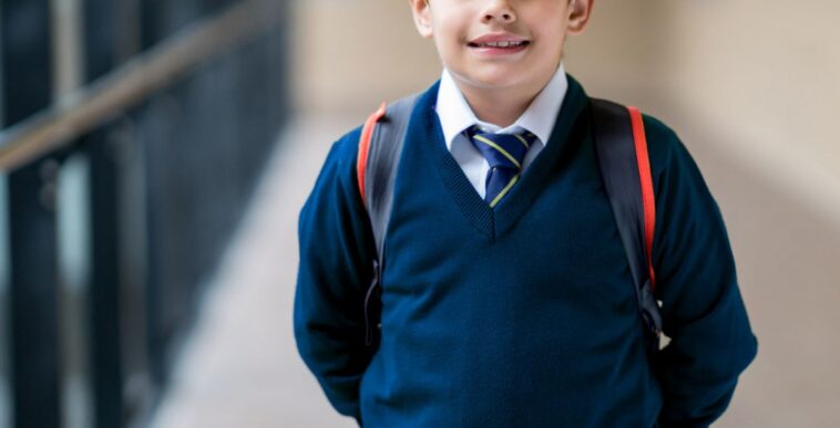 A young male student looking very happy at school wearing his uniform.