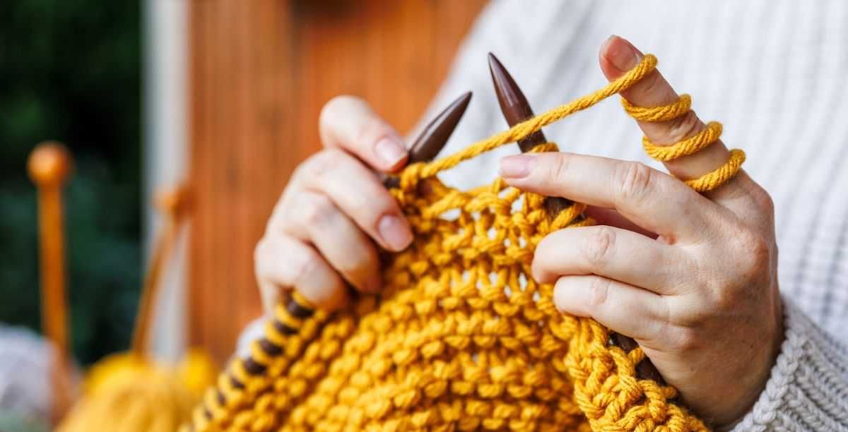 Woman in woollen sweater knits warm clothing of yellow yarn.