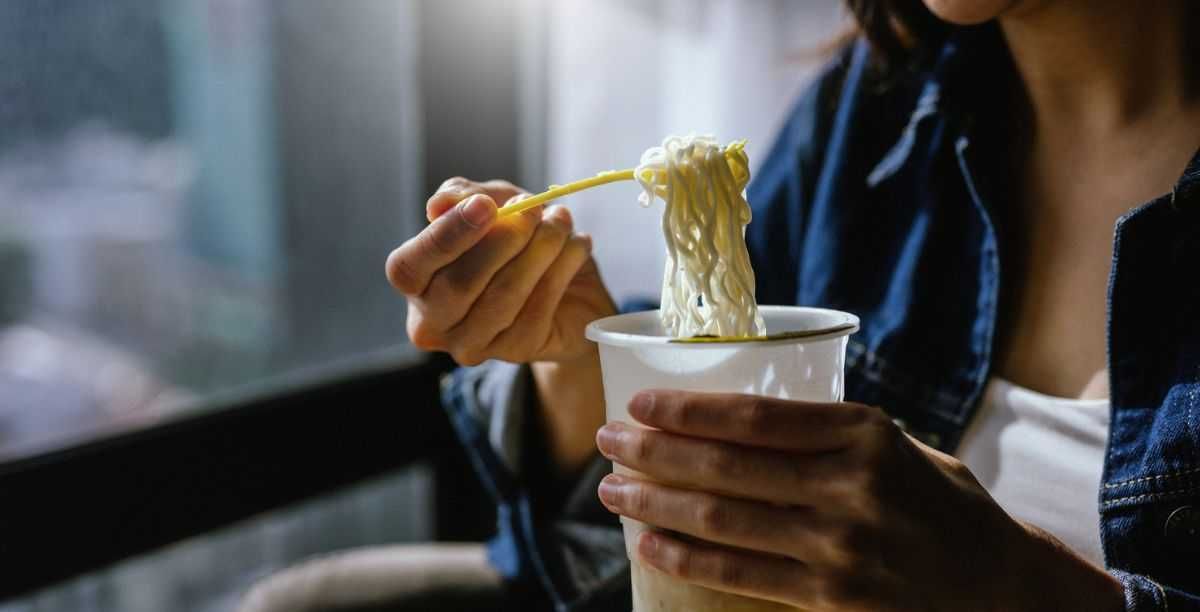 A woman is enjoying eating instant noodles in her living room at home.