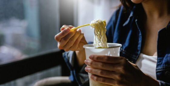 A woman is enjoying eating instant noodles in her living room at home.