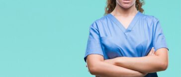 Young, brunette female doctor wearing scrubs, over isolated background skeptic and nervous, disapproving expression on face with crossed arms.