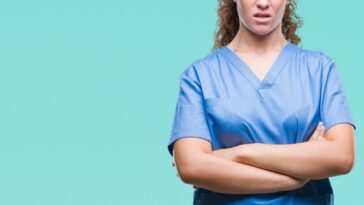 Young, brunette female doctor wearing scrubs, over isolated background skeptic and nervous, disapproving expression on face with crossed arms.