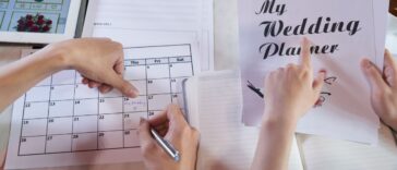 Close-up shot of unrecognizable couple wrapped up in planning wedding while sitting at table, man taking notes in calendar.